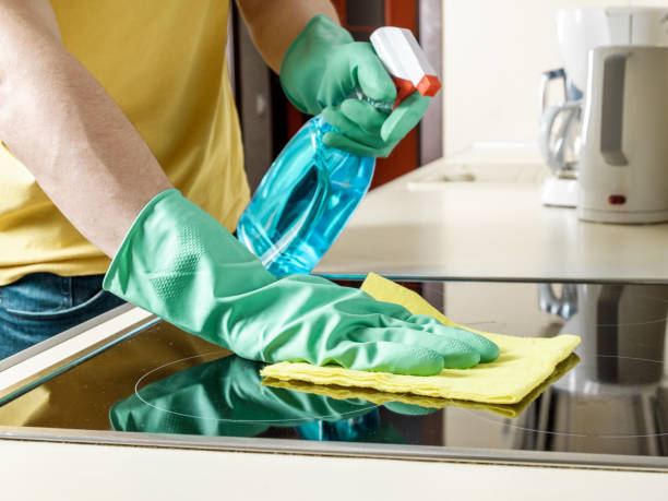 Caucasian man cleaning the cooker in the kitchen with yellow rag, spray and gloves